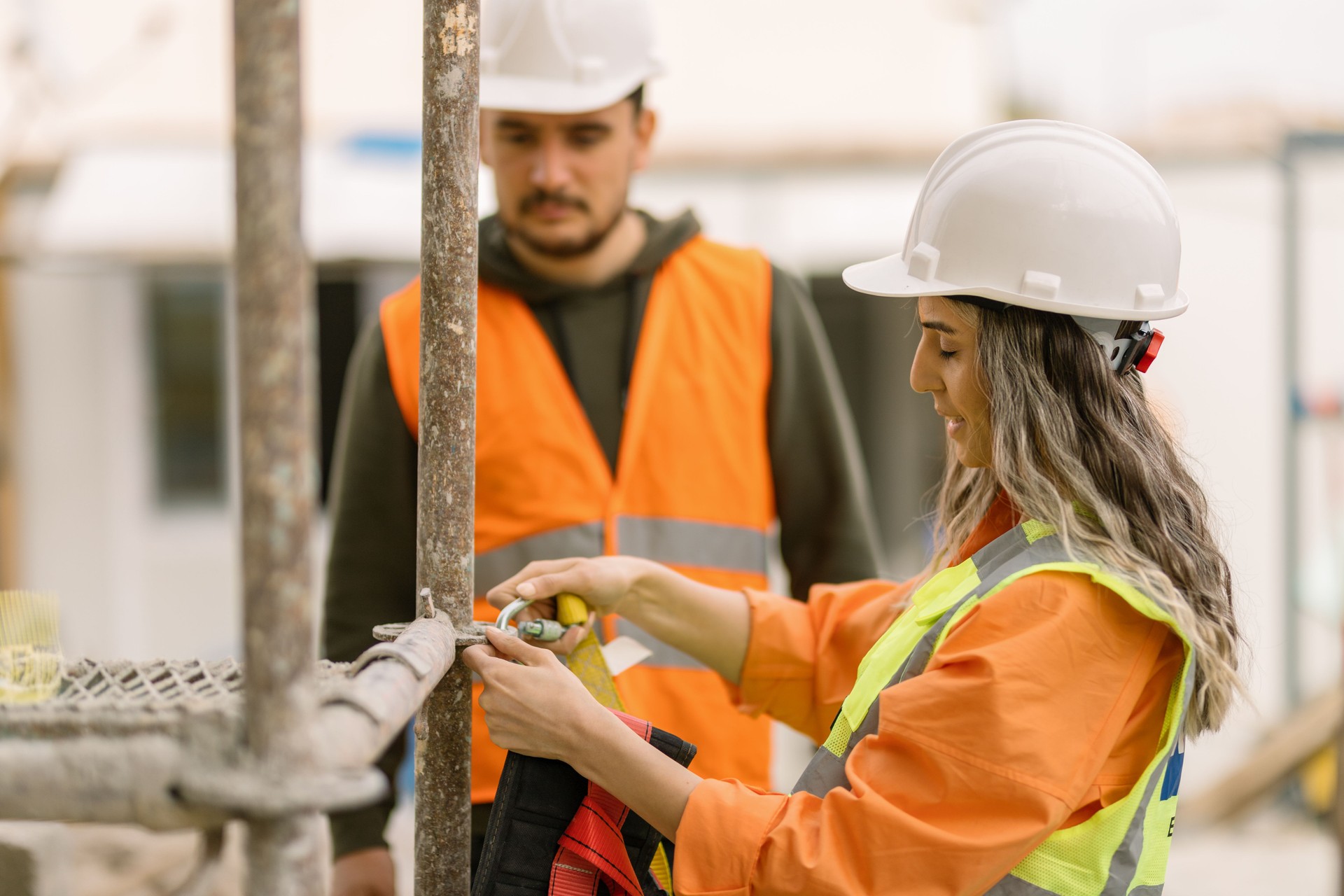 Female occupational safety specialist explaining  to construction site worker how to use  safety harness